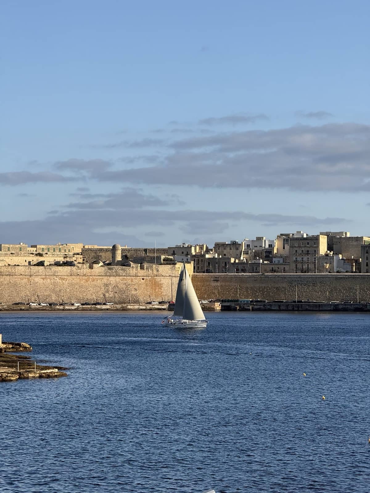 A sailboat passing beneath the bastion walls of Valletta