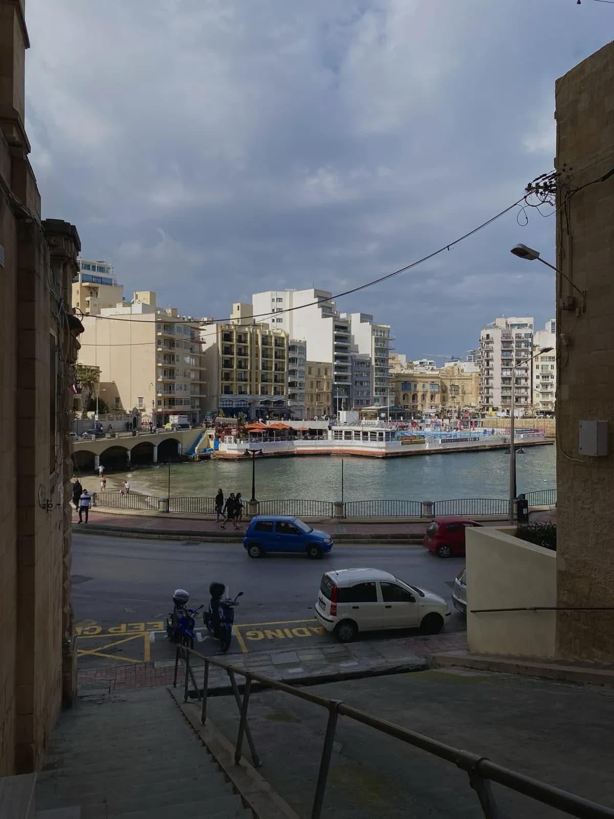 A St Julian's street sloping down to Spinola Bay, with apartment blocks and a moored boat across the water.