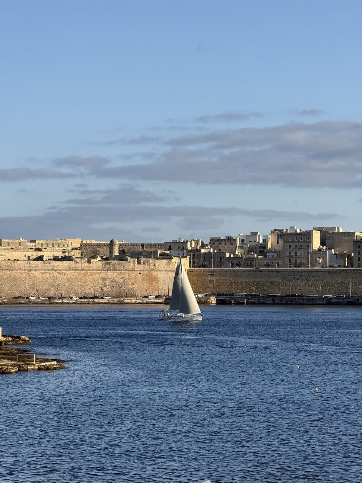 A sailboat passing beneath the bastion walls of Valletta