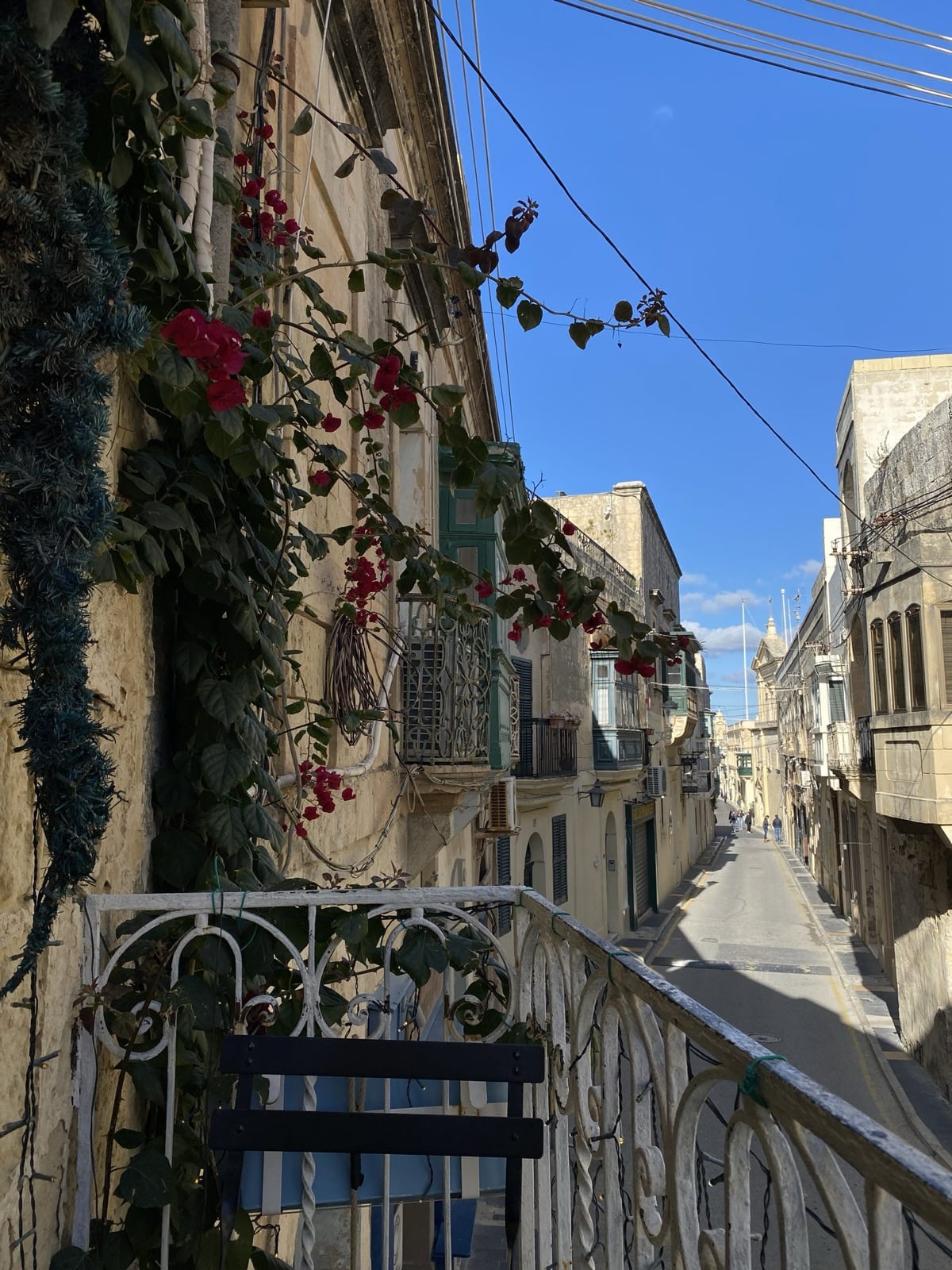 View from a balcony with bougainvillea down a long limestone street in Malta