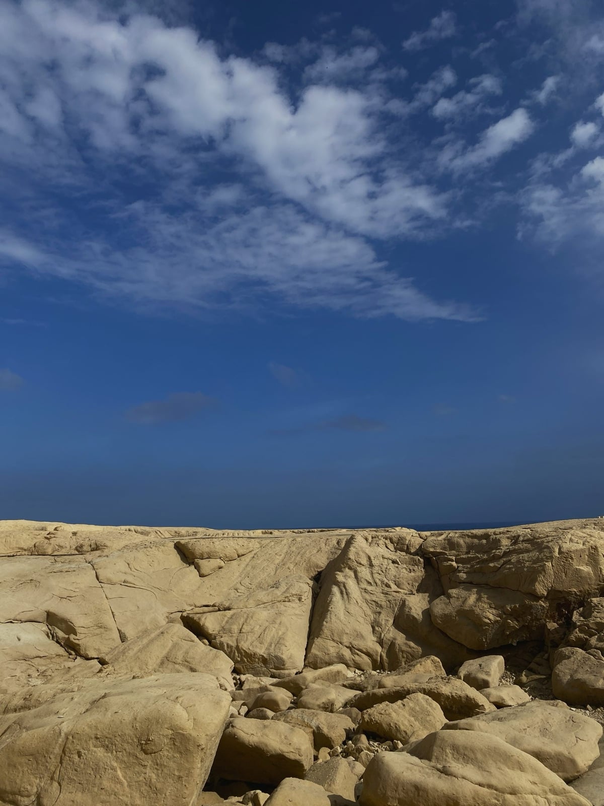 Cracked limestone rocks on the Maltese coast, with the sea on the horizon under a deep blue sky