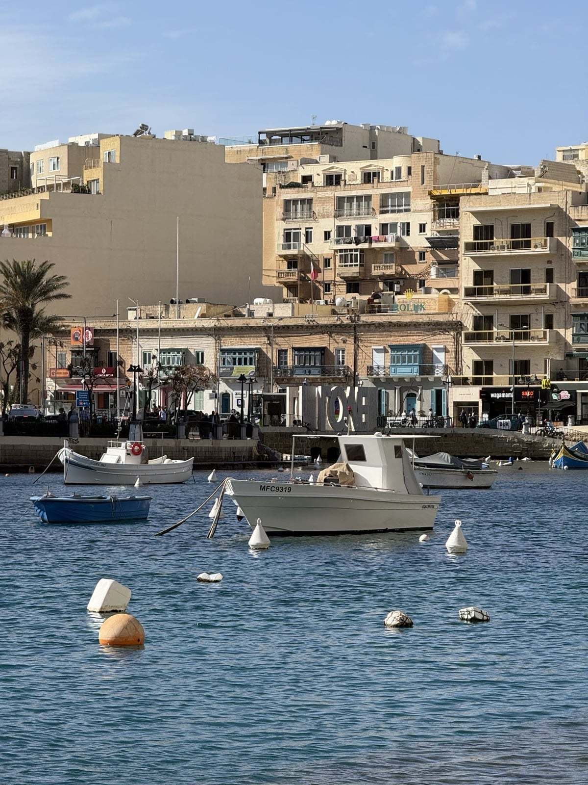 Small boats moored in Spinola Bay, St Julian's, with apartment blocks and waterfront restaurants behind