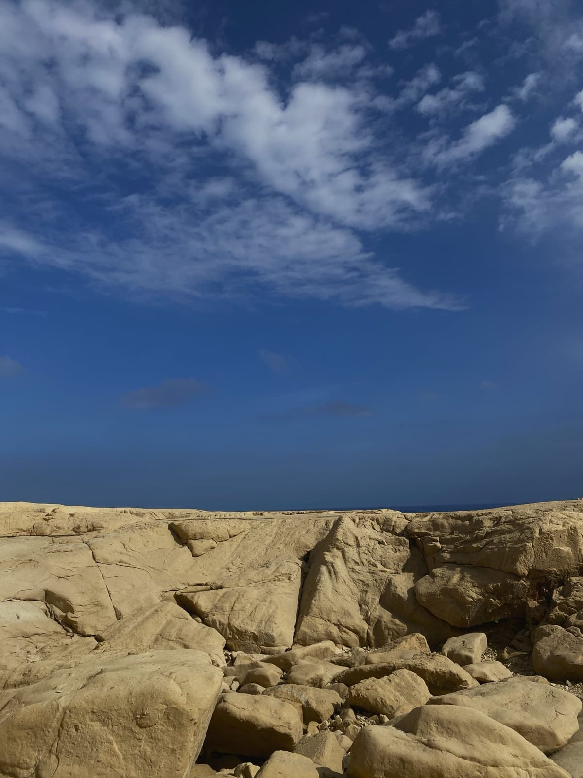 Cracked limestone rocks on the Maltese coast, with the sea on the horizon under a deep blue sky